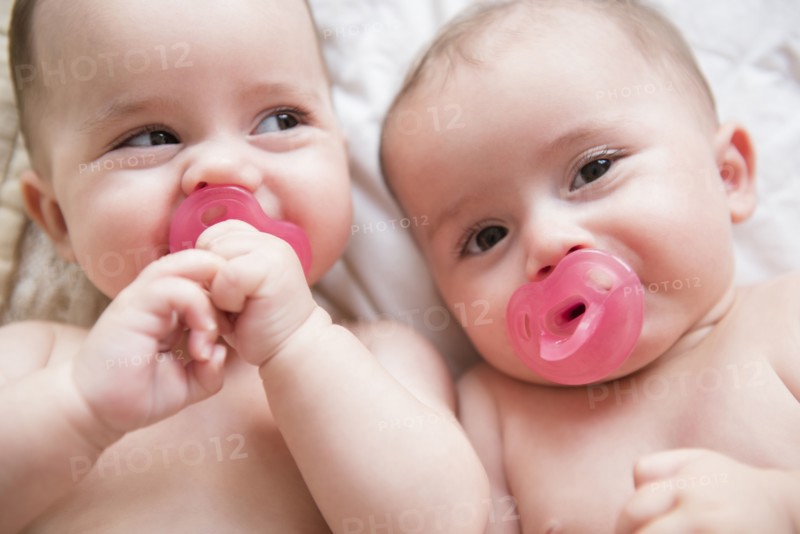 Caucasian twin baby girls sucking pacifiers