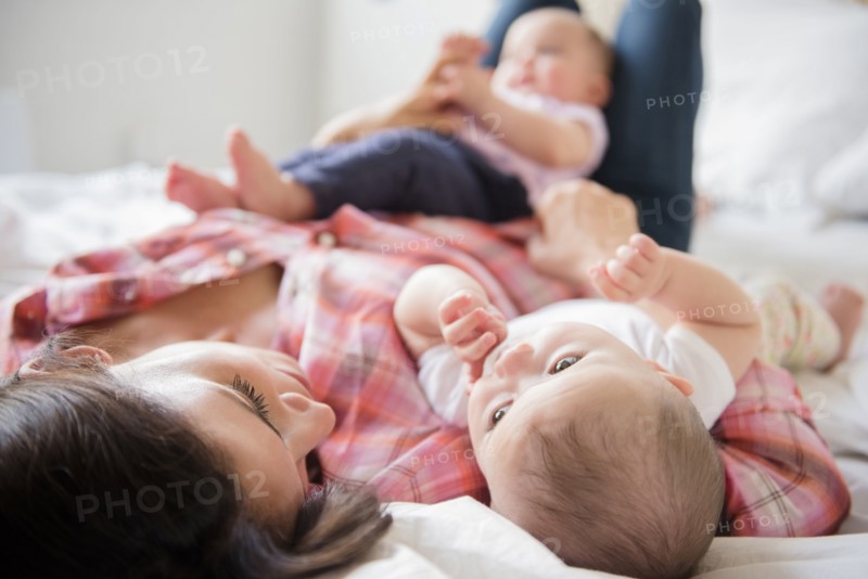 Caucasian mother laying on bed with twin baby daughters