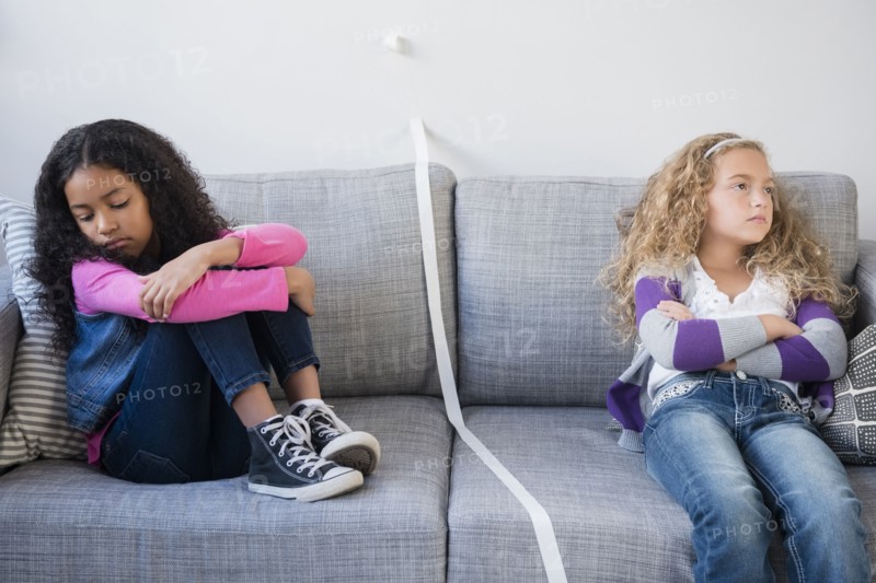 Frustrated girls dividing sofa with tape