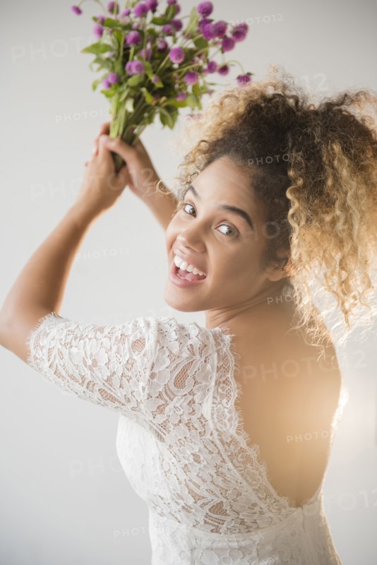 Mixed Race woman wearing wedding dress tossing bouquet
