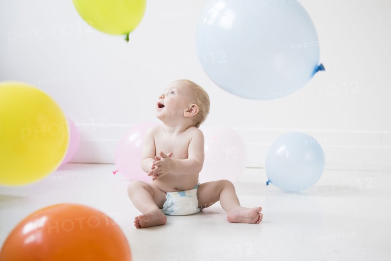 Caucasian baby boy sitting on floor watching balloons