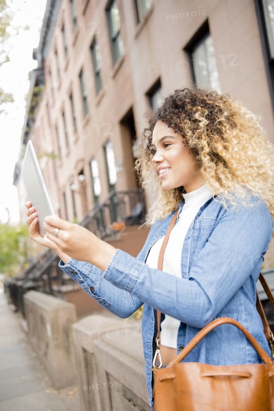 Mixed Race woman in city posing for selfie using digital tablet