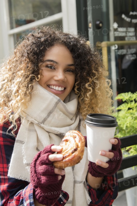 Smiling Mixed Race woman showing donut and coffee cup