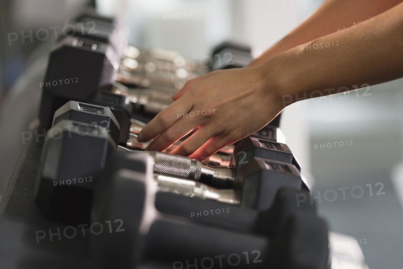 Hands of Mixed Race woman reaching for dumbbells
