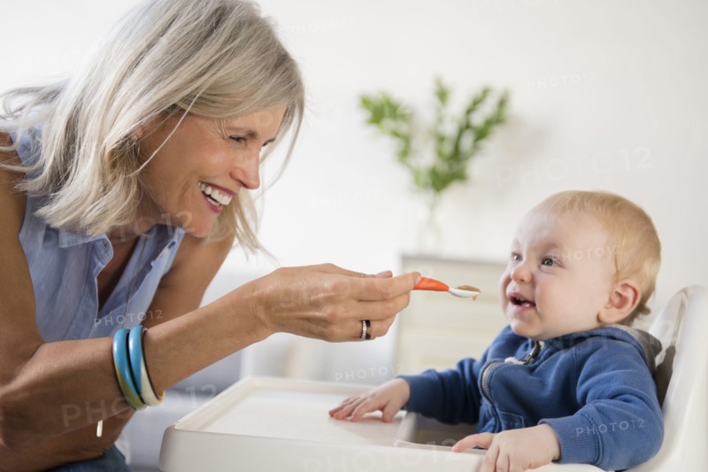 Smiling Caucasian grandmother feeding baby grandson in high chair