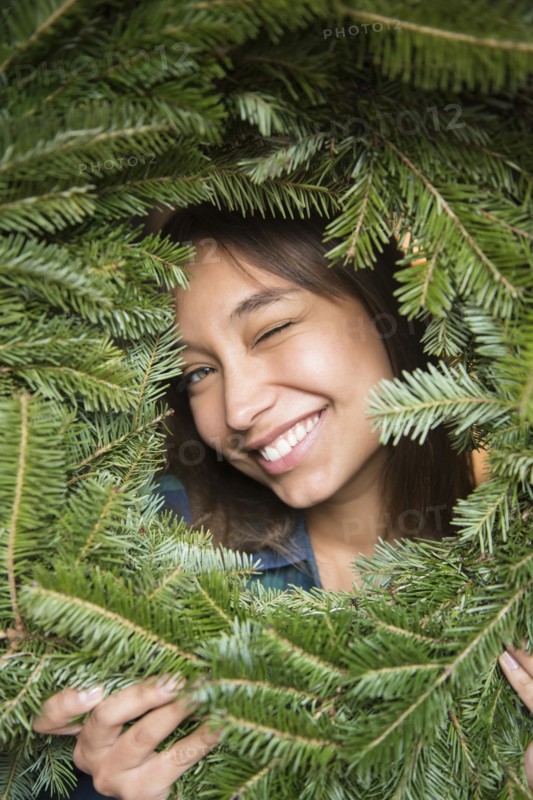 Mixed Race woman winking in pine wreath