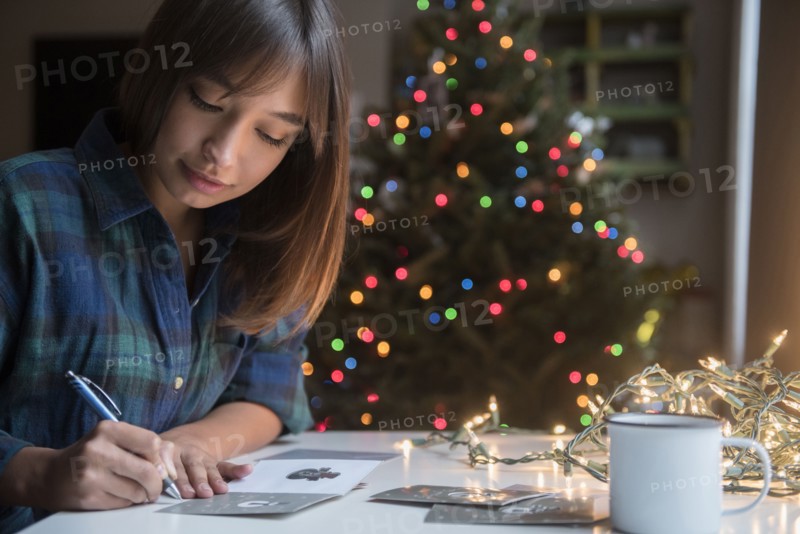 Mixed Race woman writing on card near Christmas tree
