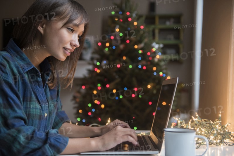 Mixed Race woman using laptop near Christmas tree