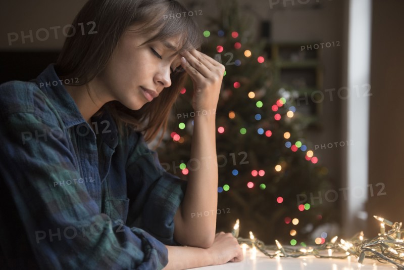 Mixed Race woman with headache near Christmas tree