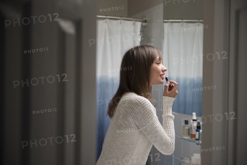 Mixed Race woman applying lipstick in bathroom