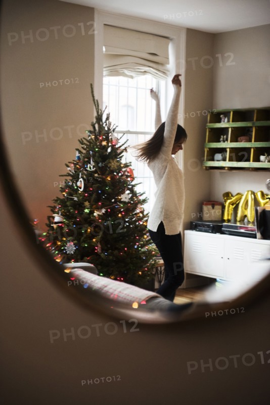 Reflection of Mixed Race woman dancing near Christmas tree