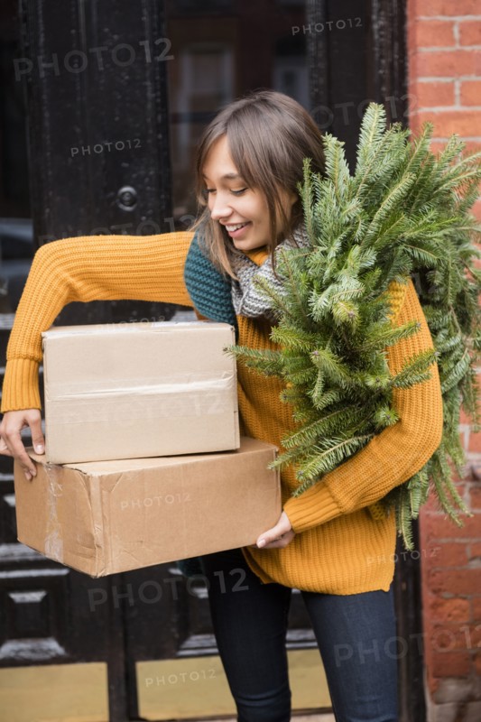 Mixed Race woman carrying pine wreath and cardboard boxes