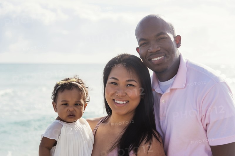 Couple posing near ocean with baby daughter