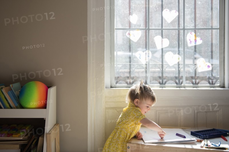 Caucasian baby girl coloring on sketchpad near window