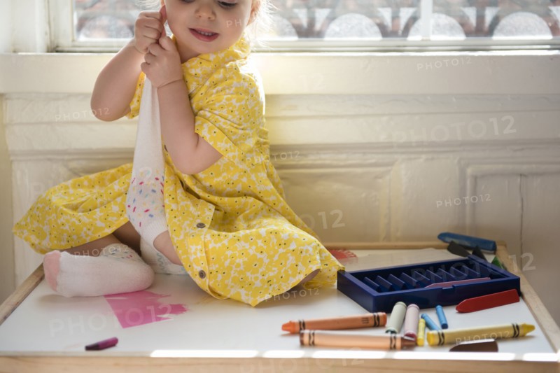 Caucasian baby girl sitting near window removing sock