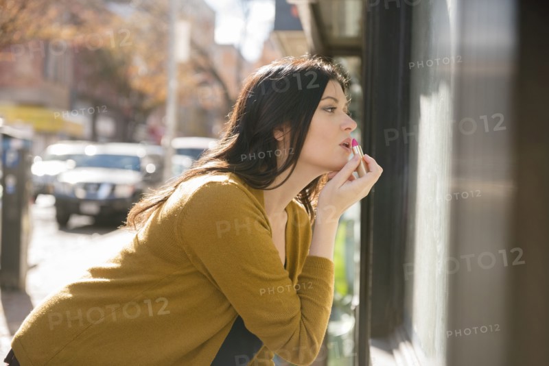 Caucasian woman applying lipstick in city