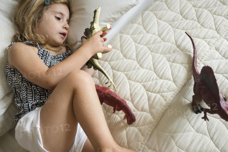 Caucasian girl laying on bed playing with toy dinosaurs