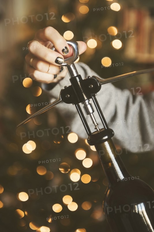 Hand of Caucasian woman opening wine bottle with corkscrew