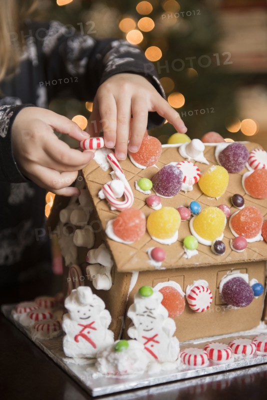 Hands of Caucasian girl decorating gingerbread house with candy