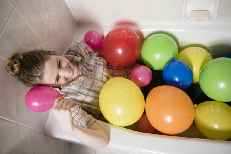 Smiling woman sitting in bathtub with multicolor balloons