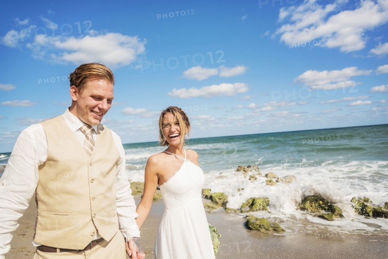 Caucasian bride and groom holding hands on beach