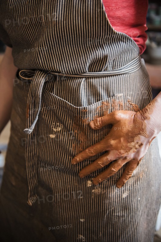 Caucasian woman wiping hands covered with pottery clay on apron