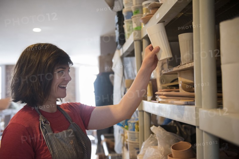Smiling Caucasian woman placing cup on shelf in workshop