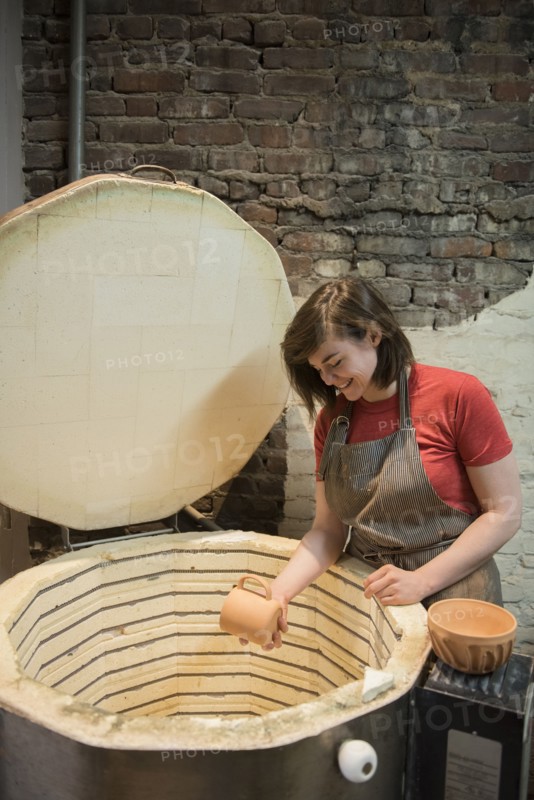 Smiling Caucasian woman placing cup in pottery kiln