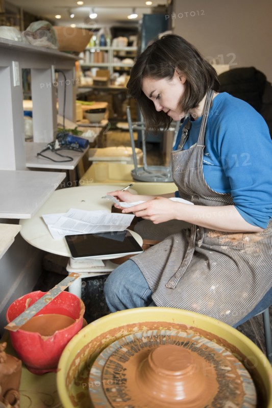 Caucasian woman reading paperwork near pottery wheel