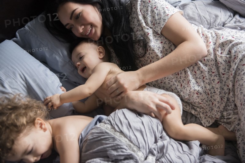 Caucasian mother playing with sons in bed