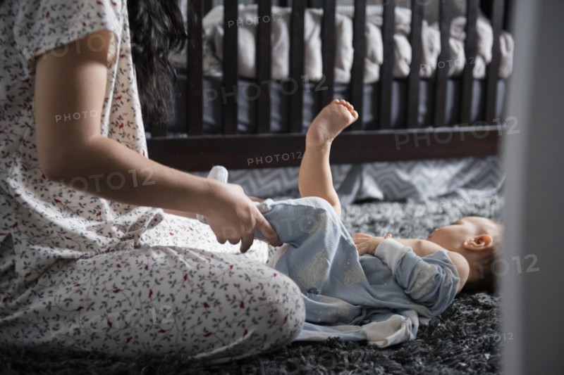 Caucasian mother dressing baby son on floor