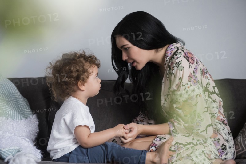 Caucasian mother sitting on sofa holding hands and talking with son