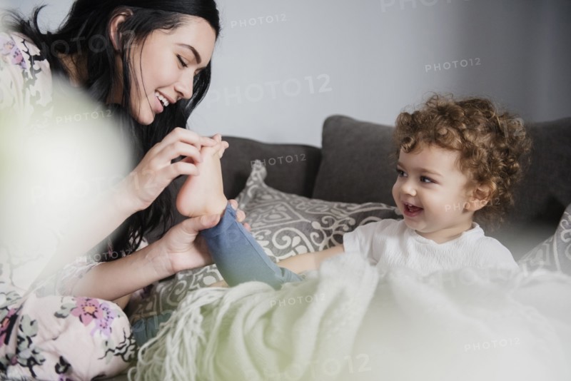 Caucasian mother sitting on sofa playing with toes of son