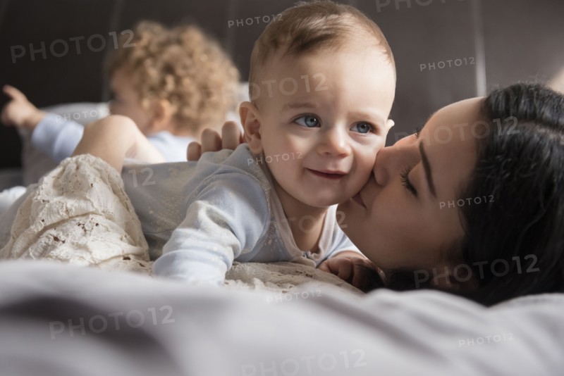 Caucasian mother laying on bed kissing baby son