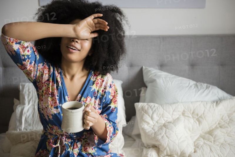African American woman sitting in bed drinking coffee