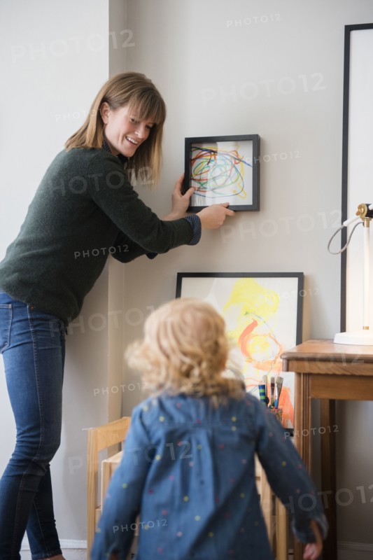 Caucasian mother and daughter hanging painting on wall