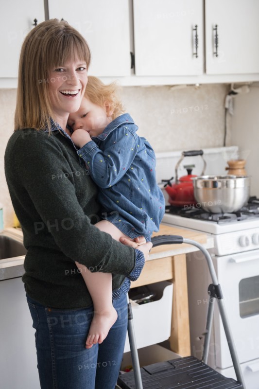 Caucasian mother holding daughter sucking thumb in kitchen