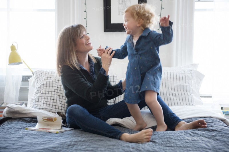 Caucasian mother sitting on bed playing with daughter