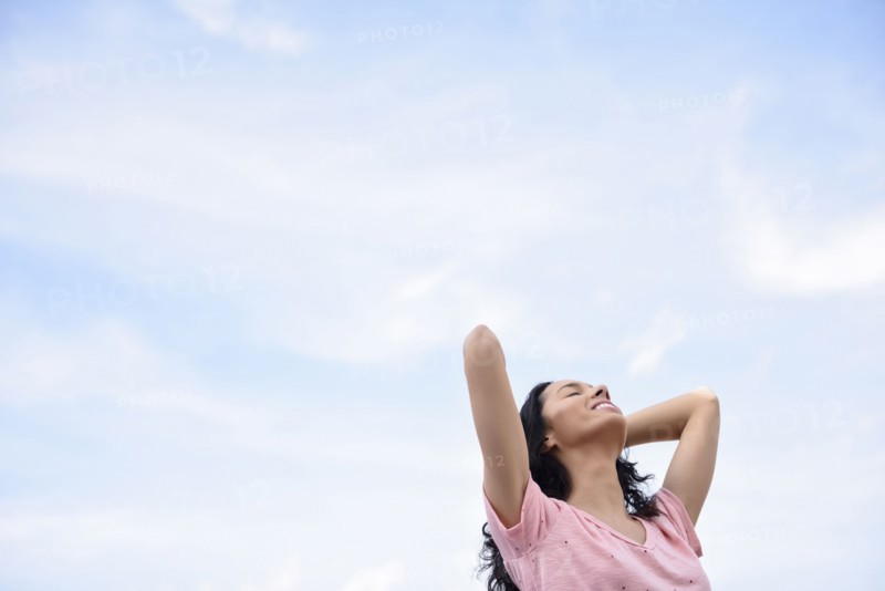 Hispanic woman with hands in hair under cloudy sky