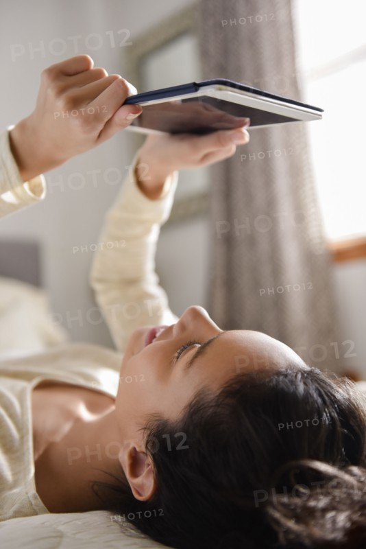 Hispanic woman laying on bed reading digital tablet