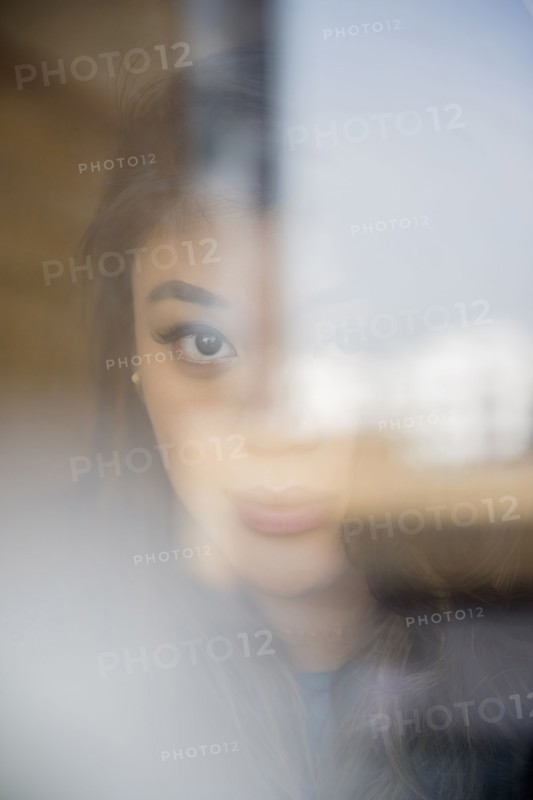 Face of serious Mixed Race woman behind window