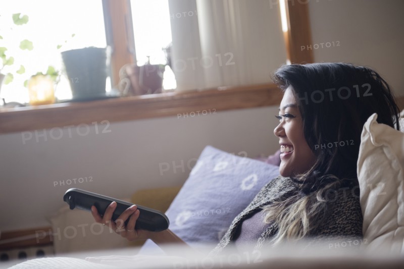 Smiling Mixed Race woman holding remote control and watching television