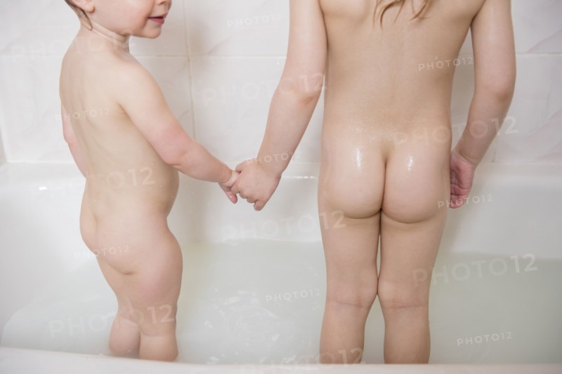 Naked Caucasian girls standing in bathtub holding hands