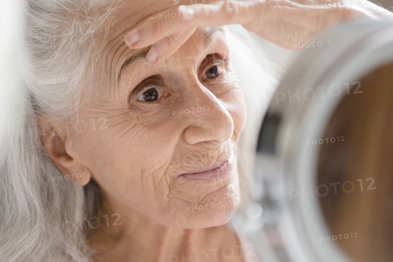 Older woman checking eye wrinkles in mirror