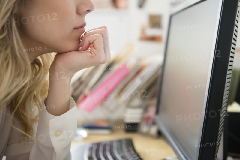 Caucasian woman with hand on chin reading computer