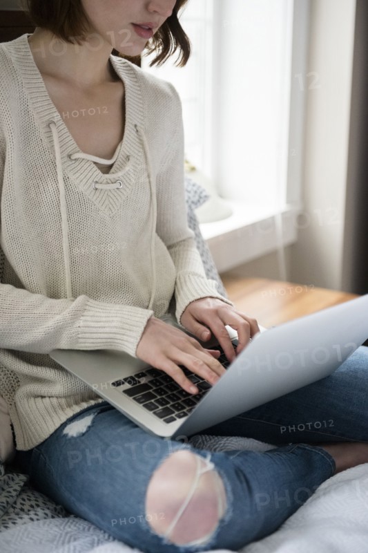 Caucasian woman sitting on bed using a laptop
