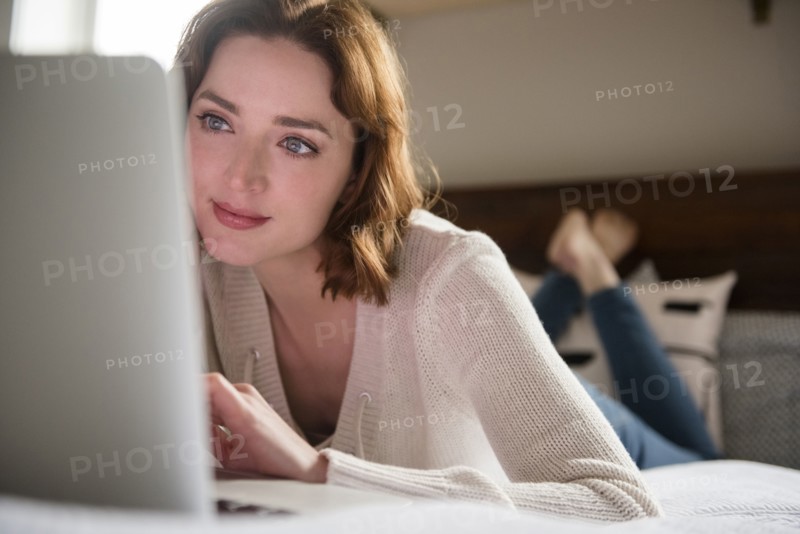Caucasian woman laying on bed using a laptop