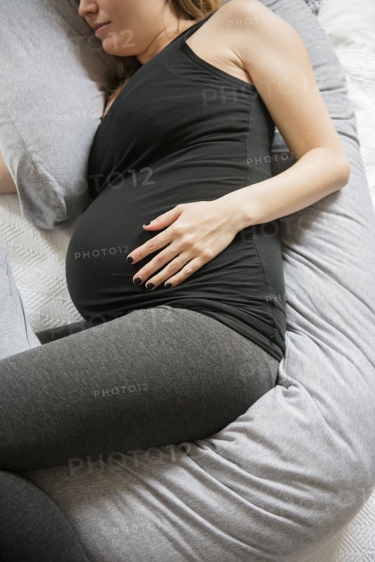 Caucasian expectant mother laying on bed with support pillow