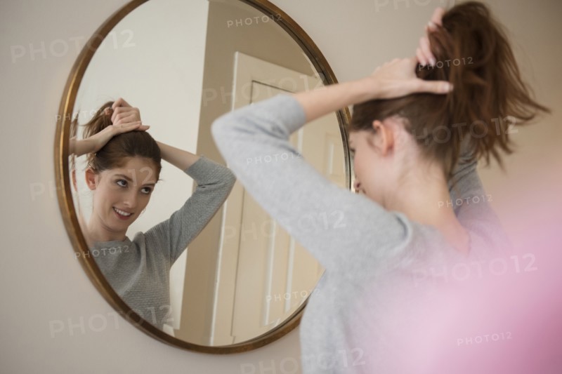 Reflection of Caucasian woman in mirror pulling back hair