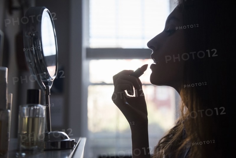 Silhouette of woman applying lipstick in mirror